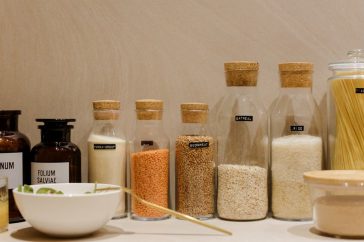 A variety of grains and pasta in labeled glass bottles displayed on a kitchen counter.